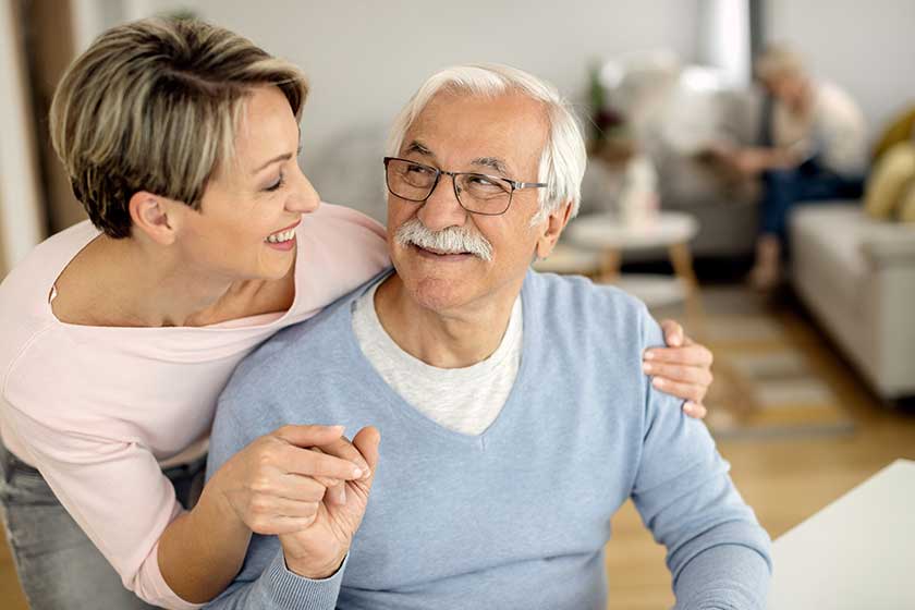 Happy woman and her senior father holding hands while communicating at home